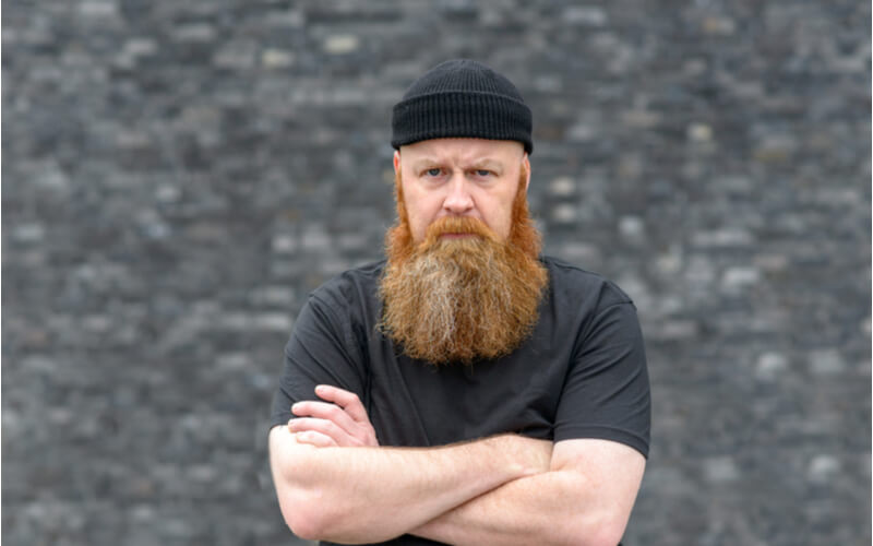 scowling bearded man knitted beanie standing with folded hand